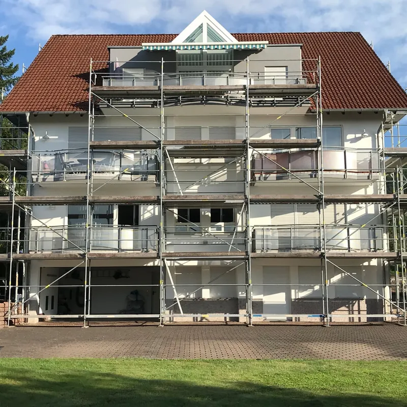 Mehrfamilienhaus mit rotem Ziegeldach, über die ganze Front eingerüstet