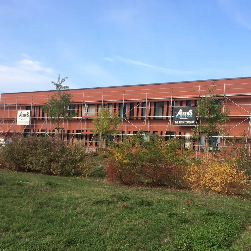 Langes zweigeschossiges Gebäude mit roter Fassade, über die ganze Länge eingerüstet